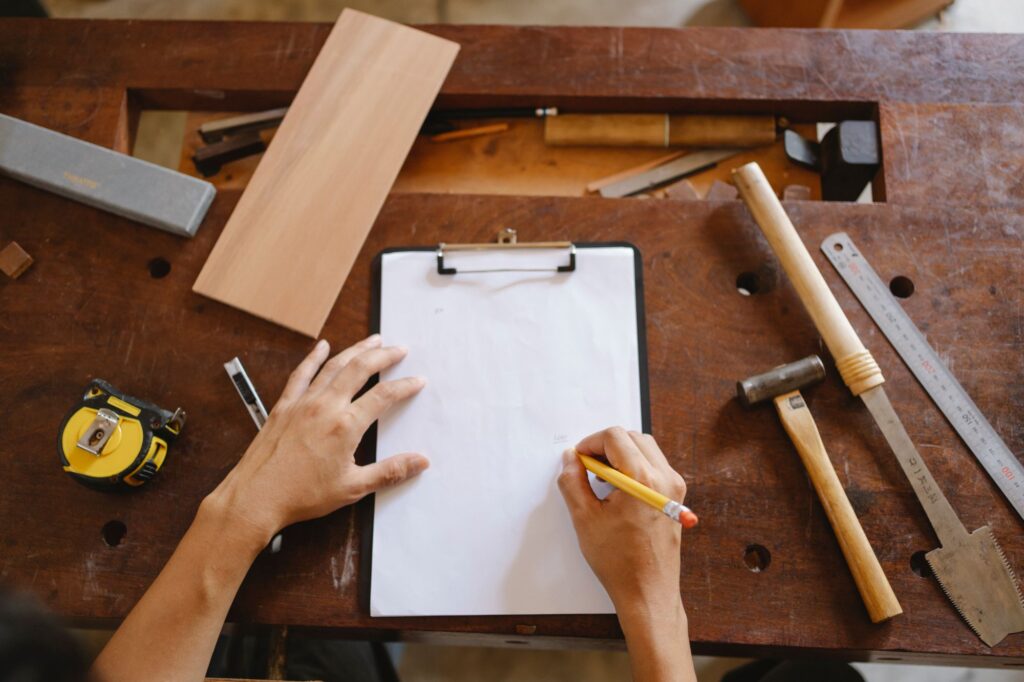 Woodworker sketching a plan on a clipboard on a workbench next to a tape measure and steel ruler
